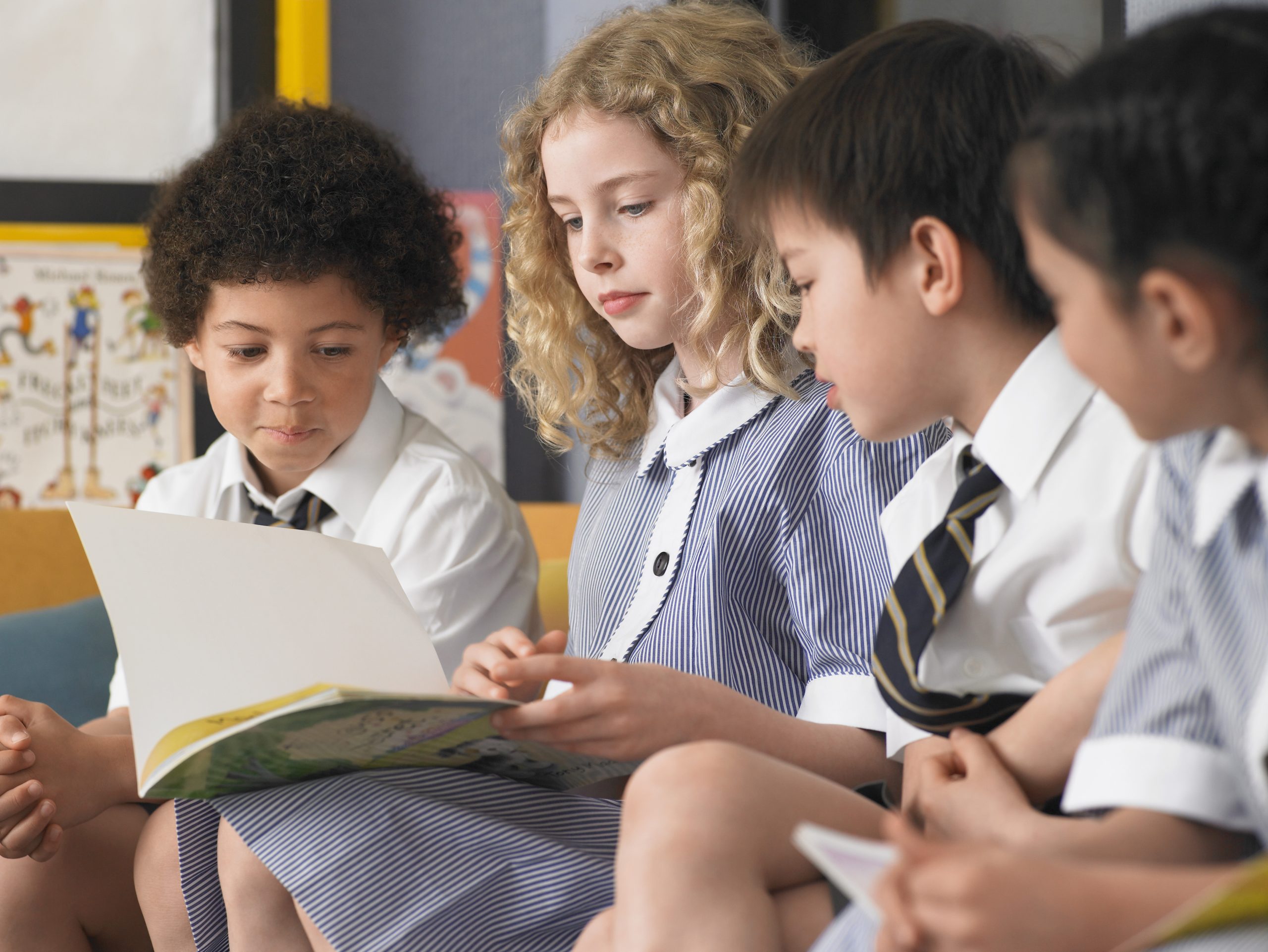 Four children sat looking at a book and wearing school uniform. 