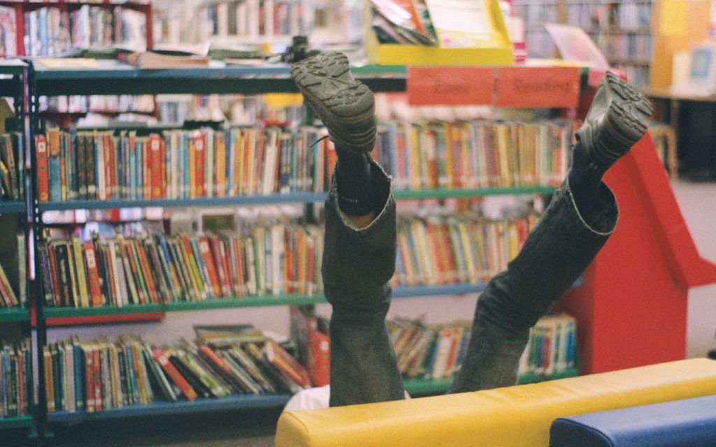 A photo of legs sticking up into the air from behind a children's seat. There are bookshelves in the background.