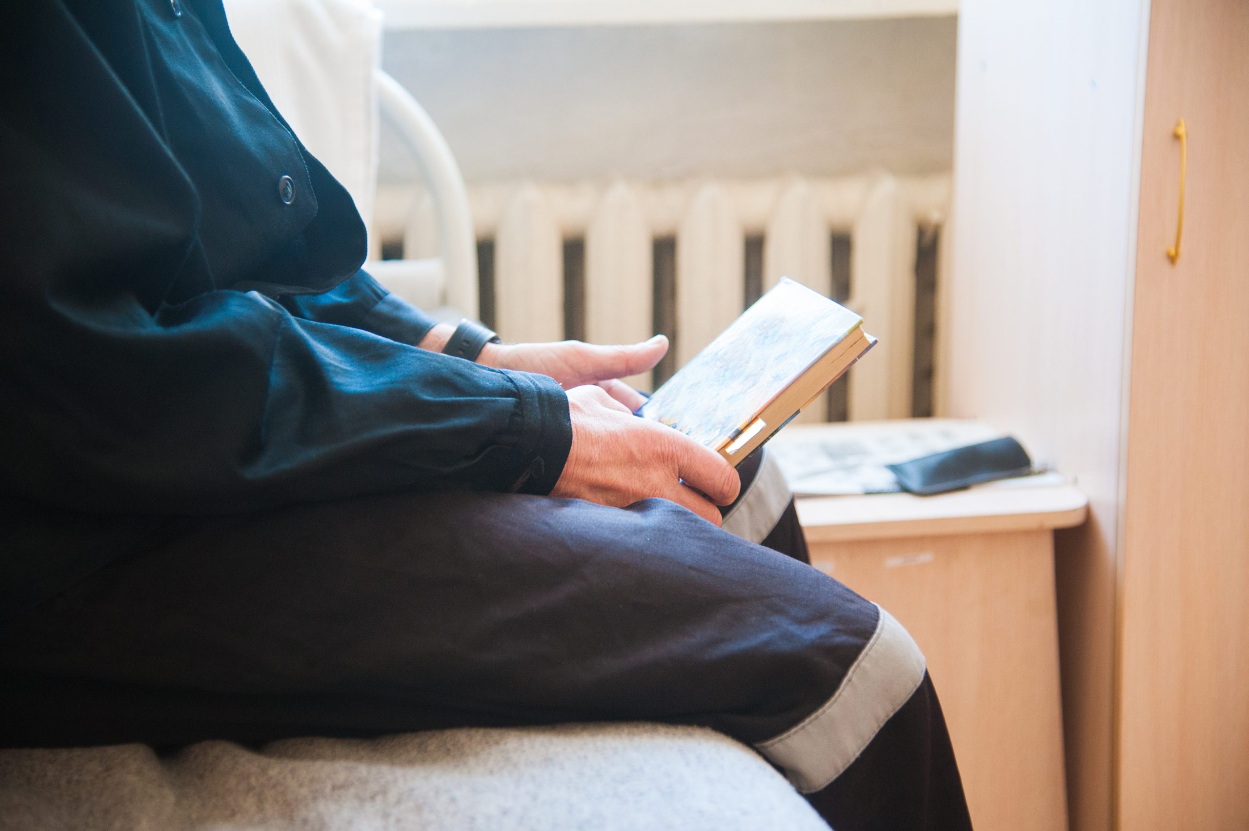 Photo of adult man reading a book in a prison cell.