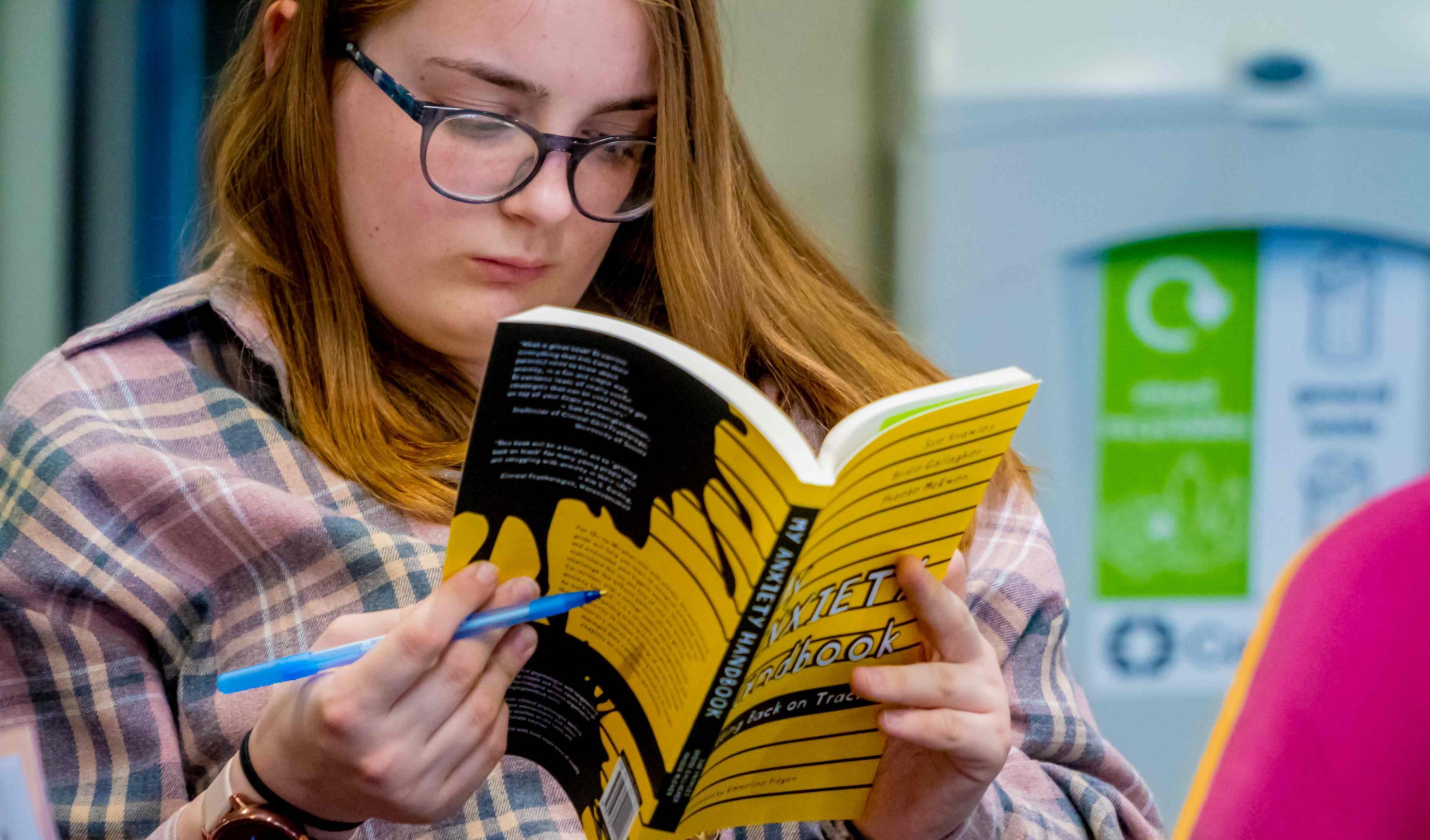 A teen girl with glasses reads a book.